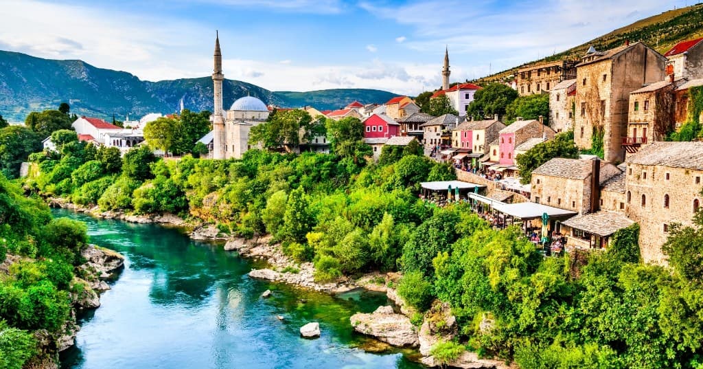 Mostar Neretva kıyısı, cami minaresi ve tarihî çatılar