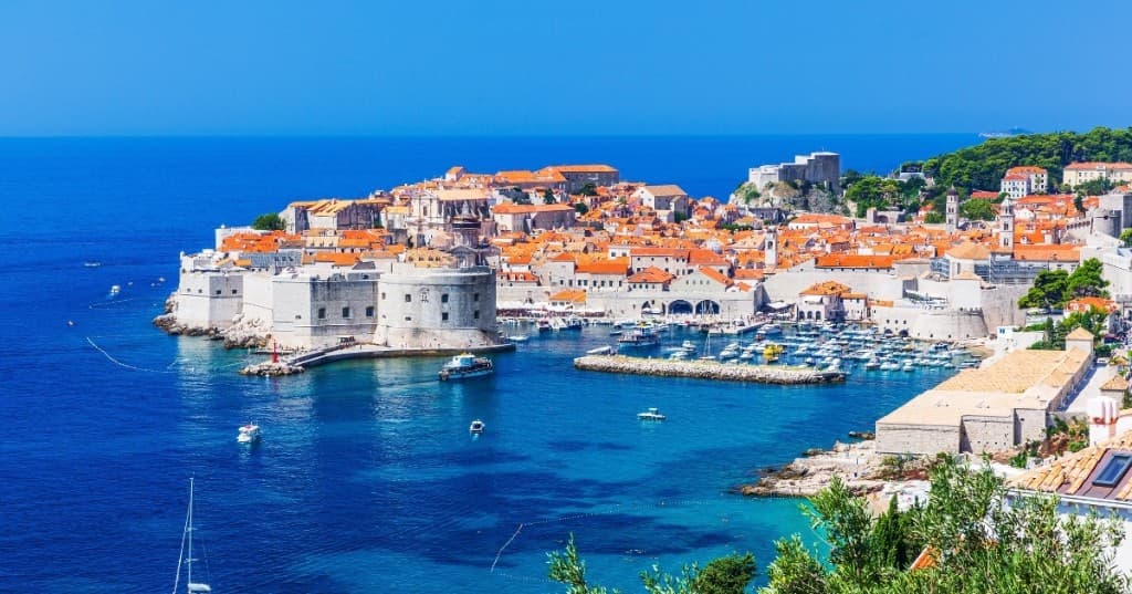 Dubrovnik eski şehir: turuncu kiremit çatılar, surlar ve Adriatik’te tekne izleri, kuşbakışı.