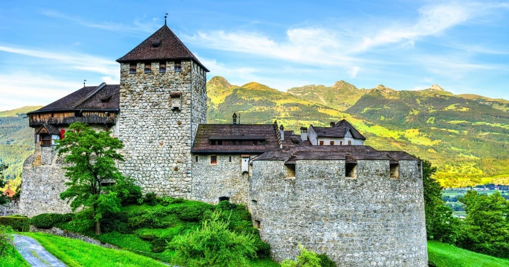 Vaduz Kalesi, yeşil yamaç ve Alp silüeti, açık gökyüzü