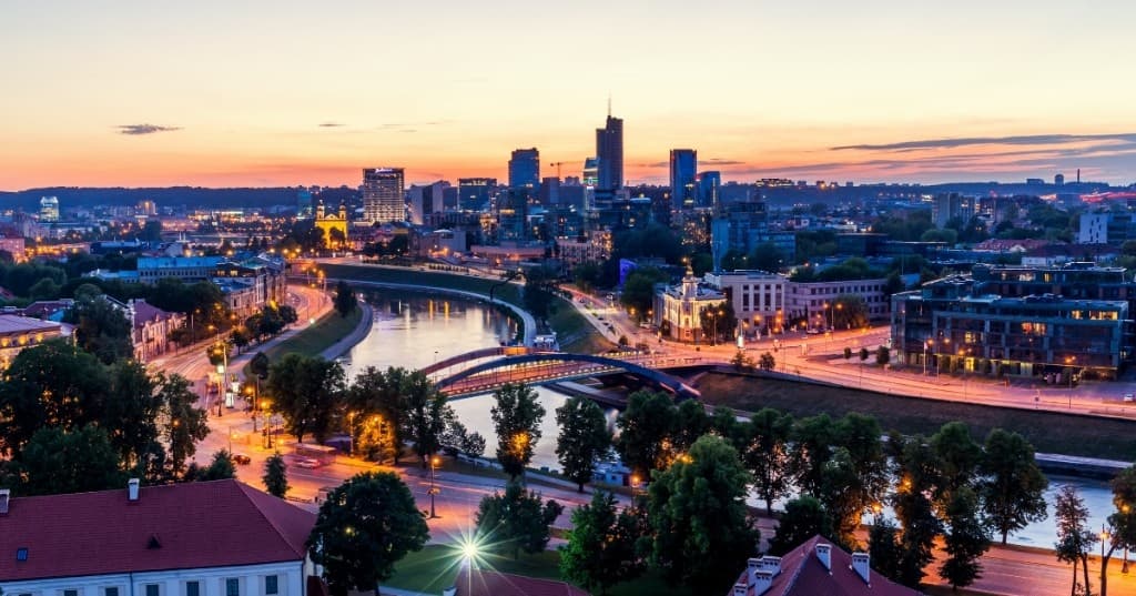 Vilnius: Neris Nehri, Mindaugas Köprüsü, kırmızı çatılı tarihî şehir ve modern gökdelenler üzerinde gün batımı.